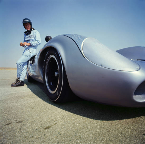 Steve McQueen in Firestone racing suit leans against a Lola T70 SL- Old Photo