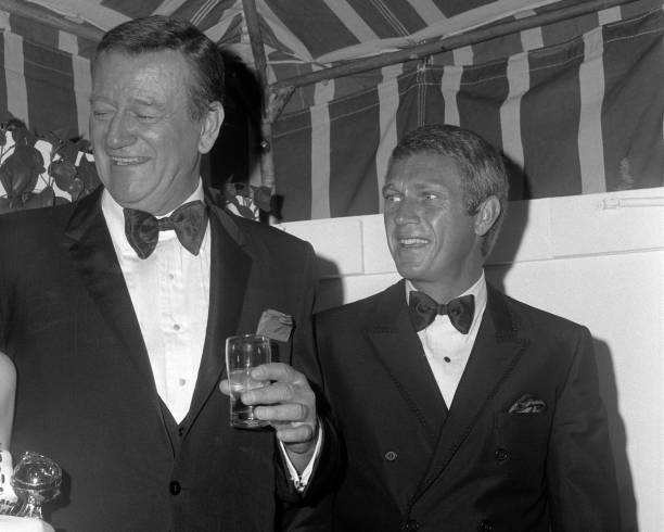John Wayne and Steve McQueen share a laugh during the 24th Annual - Old Photo 1